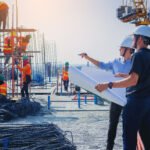 Structural engineer and architect working with blueprints discuss at the outdoors construction site.