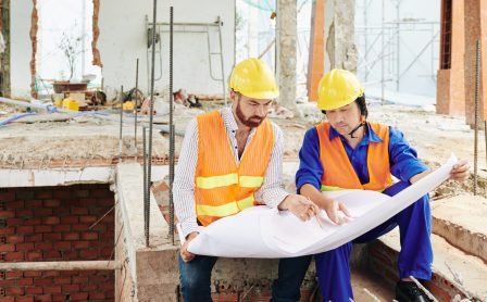 Serious multi-ethnic builders sitting in room of builing under construction and discussing blueprint